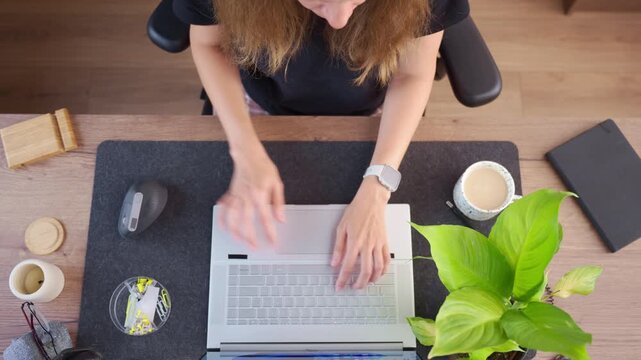 Woman works on laptop, moving computer mouse and typing on keyboard at desk