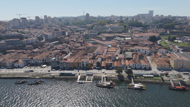 Aerial view of Marginal de Gaia along the Douro River with traditional rabelo boats, historic buildings, and urban cityscape in Vila Nova de Gaia, Porto, Portugal.