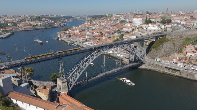 Aerial view of Luis I Bridge spanning the Douro River with a train on the upper deck and a boat below, surrounded by the historic cityscape of Porto, Porto District, Portugal.