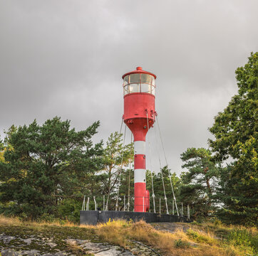 Red and white lighthouse standing among coastal trees.