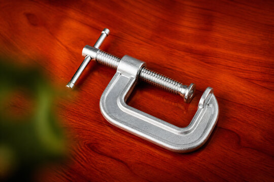 A metal clamp and screw are resting on a polished wooden surface.