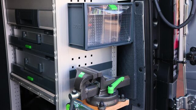 Close-up shot of professional Bott van racking system, heavy-duty bench vise, storage drawers, and organizer bins inside equipped service vehicle workspace on sunny day