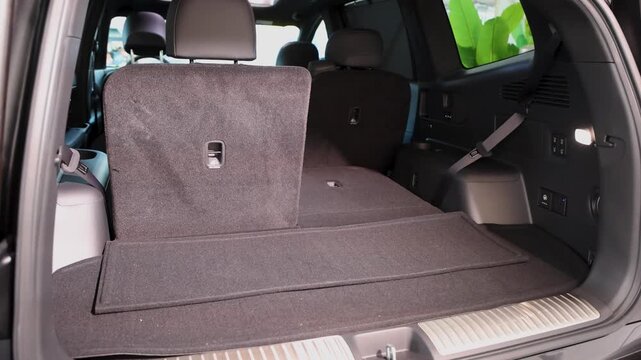 Wide shot of open trunk cargo space in modern SUV EV car showing folded third row seats, interior side panel controls, socket, and wide rear compartment at exhibition on sunny day