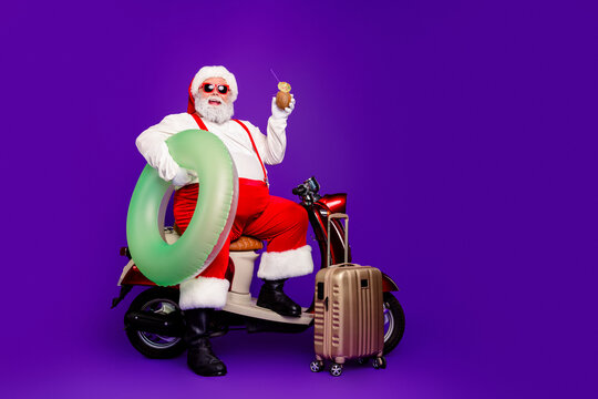 Santa Claus on scooter with inflatable swim ring, suitcase and tropical drink celebrating Christmas vacation and summer holiday