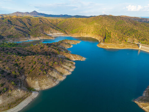 Aerial view of Dipotamos Reservoir with its deep blue water surrounded by rugged hills and dry vegetation in Dimos Lefkaron, Larnaca, Cyprus.