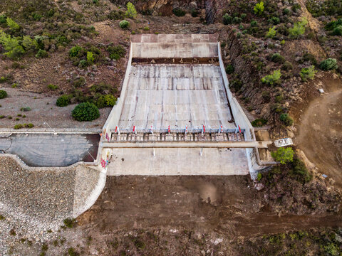 Aerial view of the concrete spillway at Dipotamos Reservoir surrounded by hills and vegetation in Dimos Lefkaron, Larnaca, Cyprus.