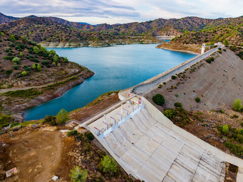Aerial view of Dipotamos Reservoir featuring the concrete dam wall and the surrounding hills and water in Dimos Lefkaron, Larnaca, Cyprus.