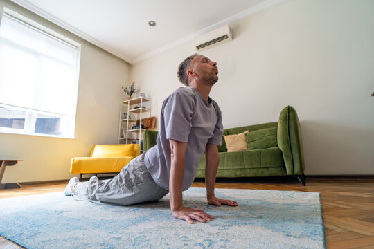Man performs back extension yoga stretch at home to improve spinal mobility and posture, open chest and hips, relieve stiffness and support daily sedentary recovery.