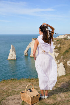 Woman with picnic basket overlooking Etretat sea arch from cliff