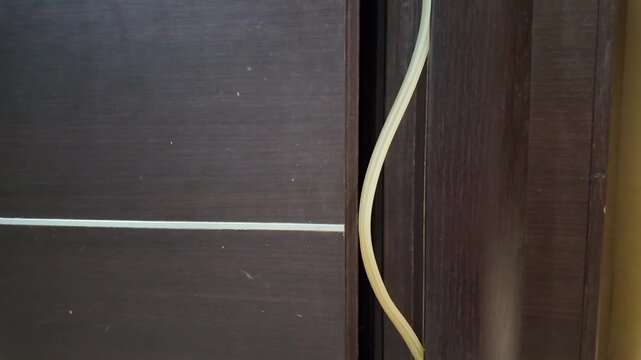 Dark wooden door with visible cable running along its edge. Cable curves gently, hinting at recent or unnoticed installation. Door shows minor signs of wear and use. No people, no animals