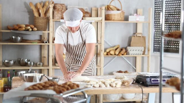 Smiling young male baker working with dough at the bakery, preparing for baking 