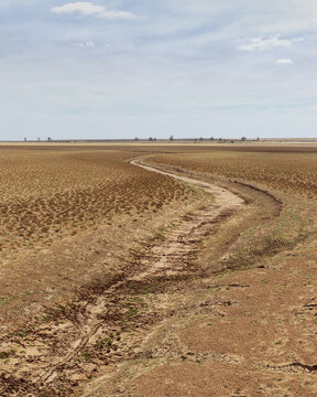 Aerial view of severe drought conditions across barren farmland with dry vegetation, cracked earth and an empty drainage channel, Central Karoo DC, Western Cape, South Africa.