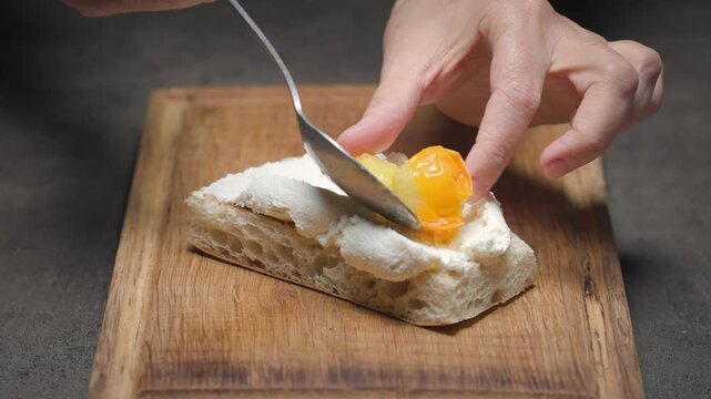 chef put roasted tomatoes on freshly toasted slice of ciabatta bread with italian fresh ricotta cheese, set on wooden cutting board on black countertop. The process of preparing