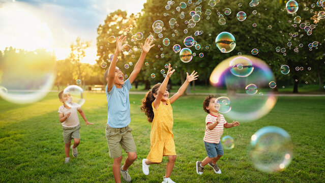 Happy children chasing and popping soap bubbles in a grassy park