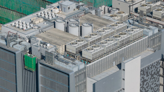 Aerial view of the rooftop of a modern building featuring rows of industrial HVAC cooling towers, large cylindrical tanks, and metal ventilation structures in Hong Kong, Hong Kong.