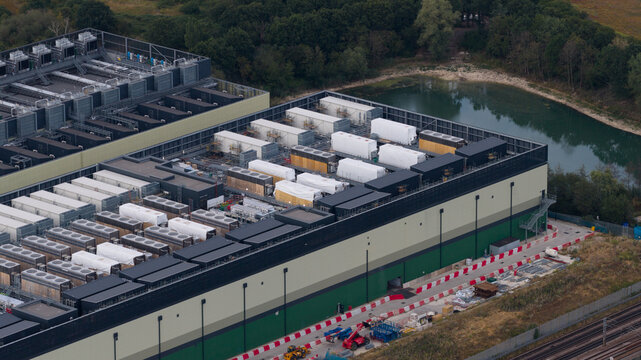 Aerial view of NTT LON1B Data Centre featuring rows of rooftop cooling units and industrial infrastructure situated next to a pond and railway tracks in Dagenham, England, United Kingdom.