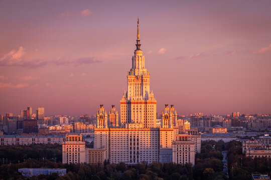 Aerial view of Moscow State University, a prominent Stalinist skyscraper, illuminated by the warm golden hour light, surrounded by urban cityscape and lush greenery in Moskva, Moskva, Russia.
