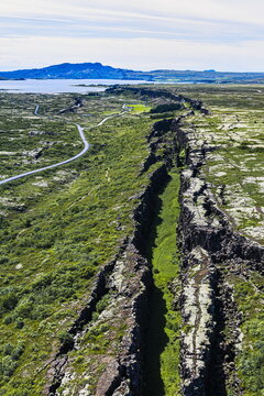 Aerial view of Almannagja gorge with its dramatic tectonic rift, rugged volcanic rock formations, and lush green vegetation in Blaskogabyggd, Iceland.