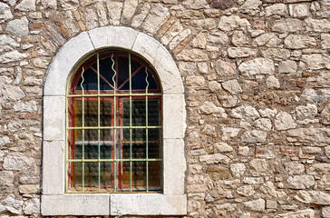 Obraz premium Single barred round arch window set in light, irregular stone wall, Patras, Greece