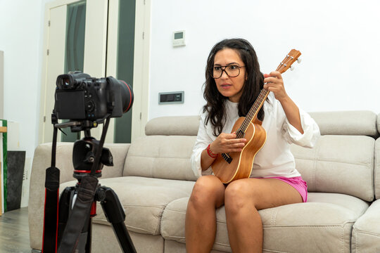 Woman playing ukulele and recording a video tutorial at home, creating content for her online channel