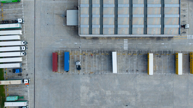 Aerial view of the TT I Cargo Line logistics facility with parked semi-trucks, trailers, and shipping containers in an asphalt parking lot in San Giuliano Milanese, Lombardia, Italy.