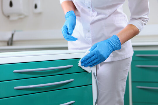 Medical worker wipes green cabinet with white cloth. Blue gloves. Clinical hygiene and disinfection