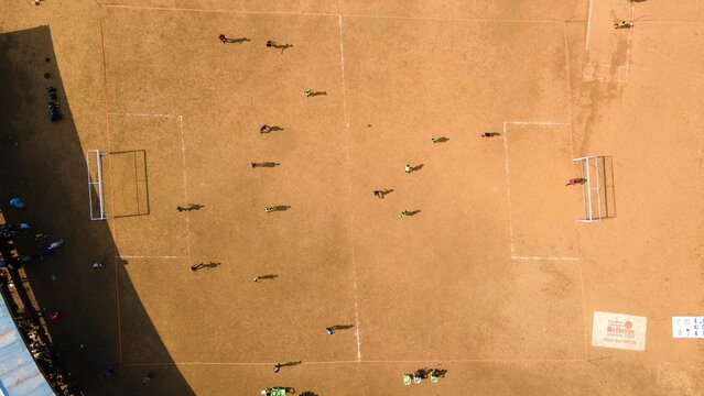 Aerial view of a soccer match being played on a dirt field with players running across the pitch in Matheran, Maharashtra, India.
