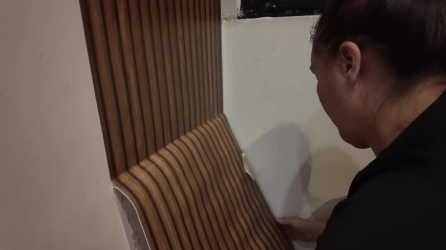 Woman adjusts vertical striped wallpaper near a window
