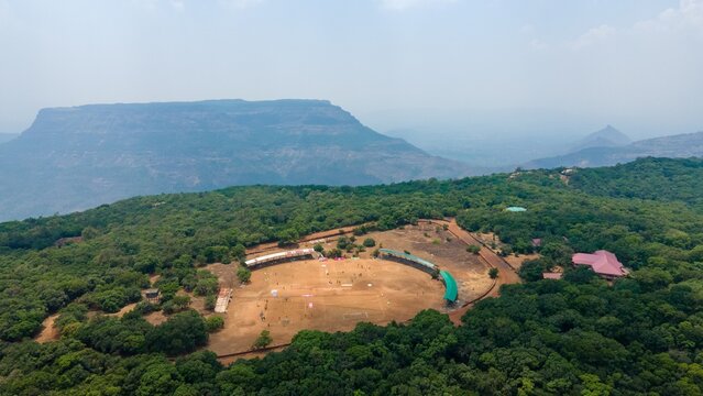 Aerial view of a cricket ground surrounded by lush green forests and hills in Matheran, Maharashtra, India.