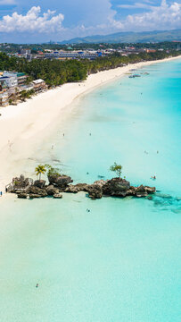 Aerial view of Willy's Rock on the white sand beach of Boracay Island with turquoise water, palm trees, and coastal buildings in Malay, Western Visayas, Philippines.