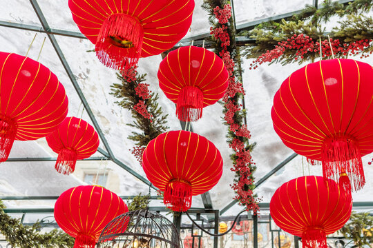 Red Chinese lanterns hang under glass roof. Festive New Year decoration with garlands and berries.