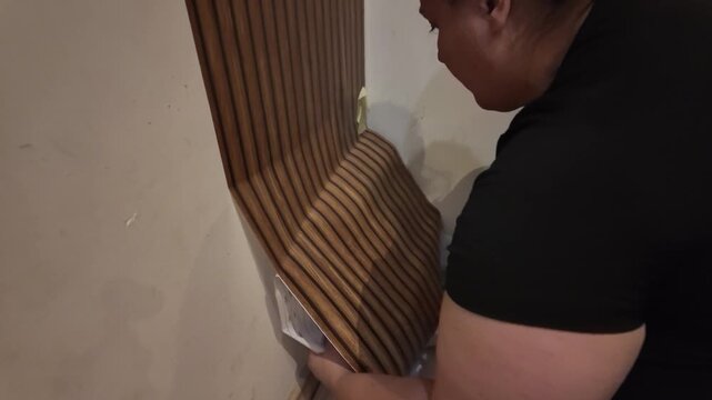 Woman applies wooden-patterned wallpaper to a wall corner