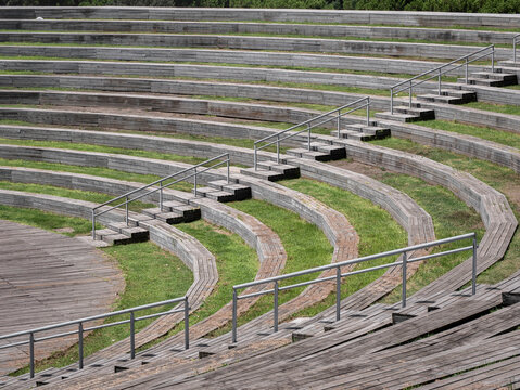 View of the open-air amphitheater in Madrid's Manzanares Linear Park, featuring curved tiered seating with wooden benches and interspersed green spaces, as well as staircases with railings