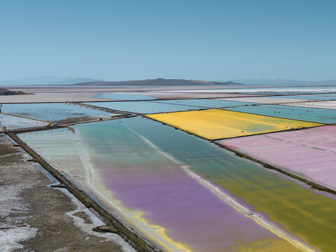 Aerial view of solar salt evaporation ponds with vibrant yellow, pink, and green water in the Great Salt Lake near Ogden, Utah, United States.