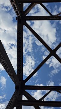 View of clouds moving in blue sky through steel girders of bridge background vertical video