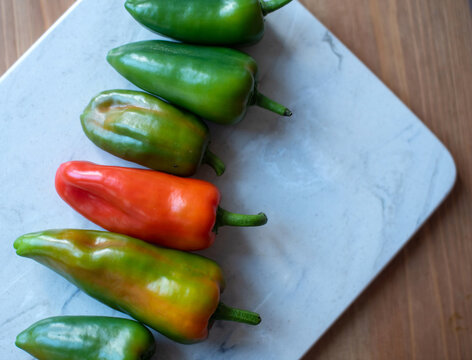 A row of fresh jalapeno peppers on a marble cutting board. The peppers vary in color from green to red, showcasing their ripeness and freshness.