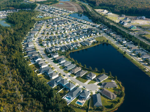 Aerial view of a residential community with identical suburban houses, winding streets, and a large retention pond in Jacksonville, Florida, United States.