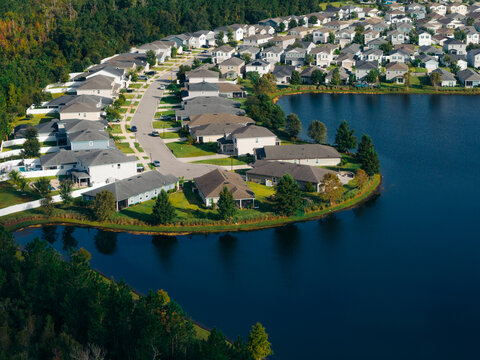 Aerial view of a suburban residential community with identical houses, a winding road, and a lake surrounded by trees in a modern housing development. Jacksonville, Florida, United States.