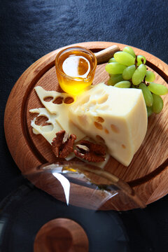 Cheese with holes, green grapes, honey jar, walnuts, wooden board, inverted glass cloche on dark background