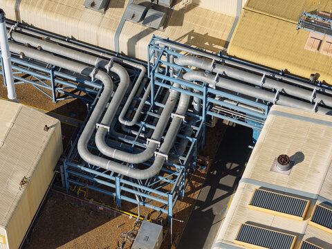 Aerial view of industrial piping systems and metal support structures on the roof of a factory facility in the United Kingdom.