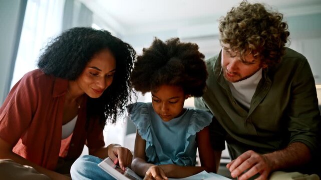 Parents pointing picture book with daughter. Multiracial family reading home.