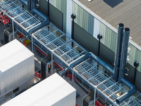 Aerial view of a data center facility featuring industrial piping, cable trays, and HVAC equipment with a worker in high-visibility gear in United Kingdom.