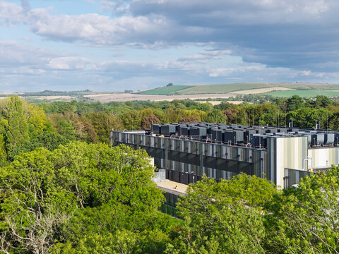 Aerial view of a modern data center facility surrounded by lush green trees and rolling hills in the United Kingdom.