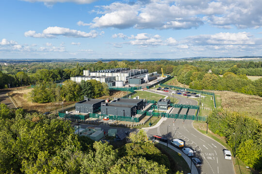 Aerial view of a modern data center facility surrounded by lush green trees and rolling hills in the United Kingdom.