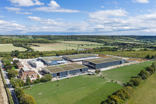 Aerial view of a large data center complex under construction, featuring modern industrial buildings with green roofs, surrounded by expansive green fields and rural landscape in the United Kingdom.