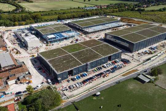 Aerial view of a large data center construction site featuring multiple modern buildings with green roofs, construction vehicles, and rows of parked cars in the United Kingdom.