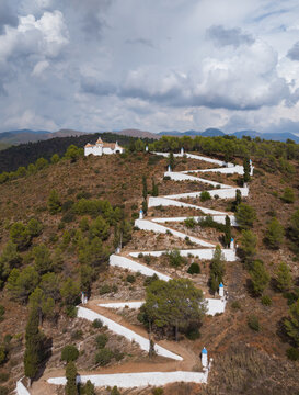 Aerial view of the Hermitage of Saint Anthony perched on a hilltop with a winding white path, surrounded by pine trees and hills in Sot de Ferrer, Comunidad Valenciana, Spain.