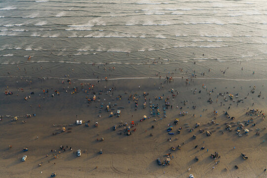 Aerial view of Clifton Beach at sunset with people walking along the sandy shore, small stalls, and vehicles parked on the beach in Karachi, Sindh, Pakistan.