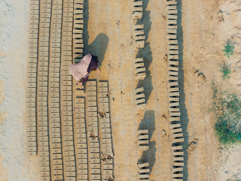 Aerial view of a worker arranging rows of mud bricks to dry in the sun at a traditional brick factory in Lahore, Punjab, Pakistan.