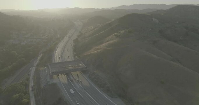 Drone shot over busy highway and overpass in backlit hazy hills